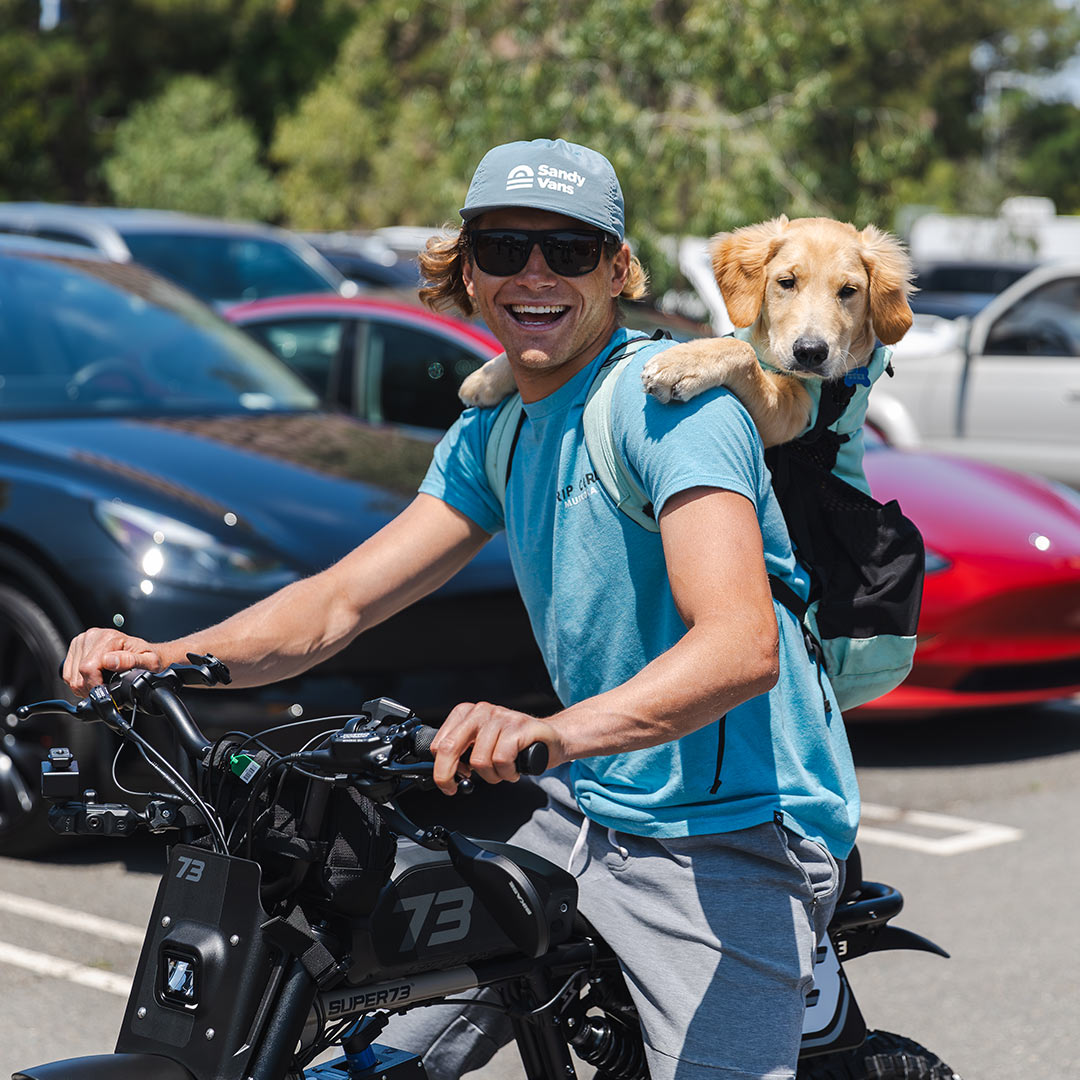 smiling man on a super73 carrying a cute dog on his bakck